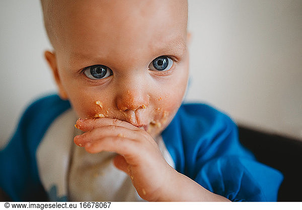 Close up of beautiful baby with blue eyes eating with his hands