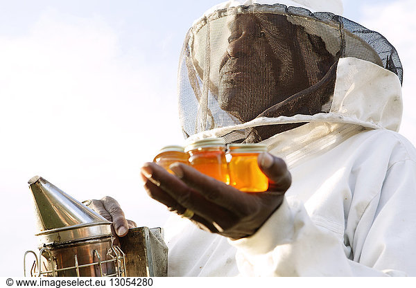Close-up of beekeeper holding smoker and honey in jars