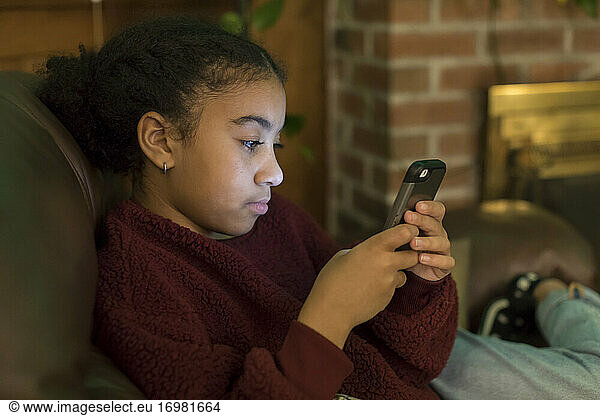 Close-up of biracial eleven year-old girl indoors staring at phone