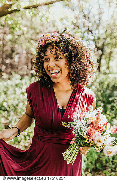 Close up of black woman smiling in wooded area while holding flowers