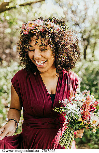 Close up of black woman smiling in wooded area while holding flowers