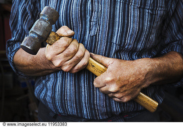 Close up of blacksmith's hands gripping a large hammer.