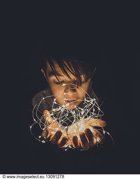 Close-up of boy holding illuminated string lights in darkroom