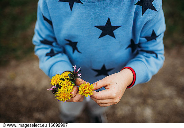 Close up of boy holding yellow flowers outside on a cold day in spring