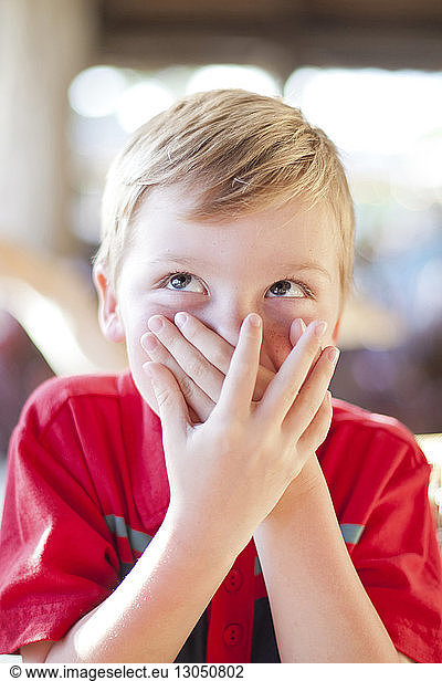 Close-up of boy looking up while covering mouth at home
