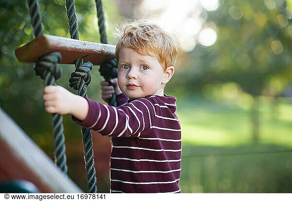 Close up of boy 3-4 years old climbing ladder on playlet in backyard