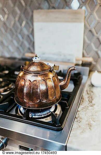 Close up of brass tea kettle heating up on gas stove in kitchen