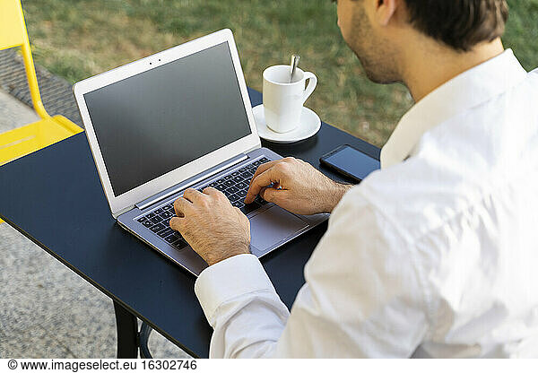 Close-up of businessman working over laptop on table at sidewalk cafe