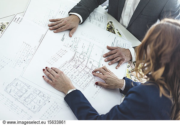 Close-up of businesswoman and businessman working on plan on desk in office