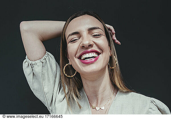 Close-up of cheerful beautiful woman with eyes closed against black background