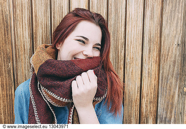 Close-up of cheerful woman standing against wooden wall