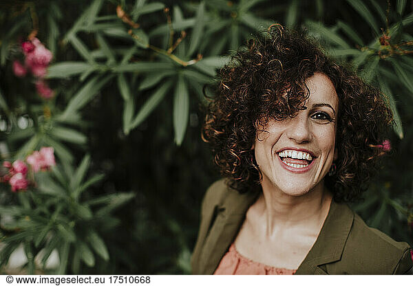 Close-up of cheerful woman with curly hair against plants in park