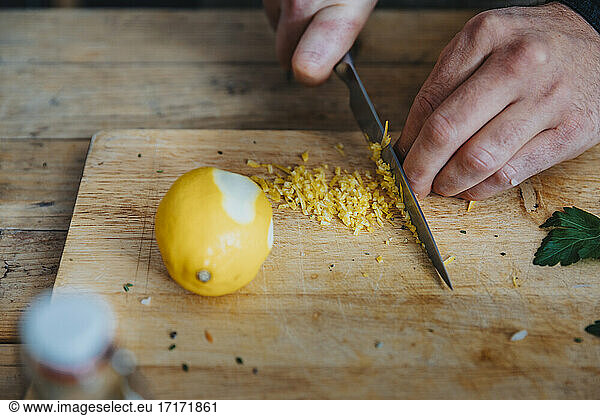 Close-up of chef cutting lemon peel on cutting board in kitchen
