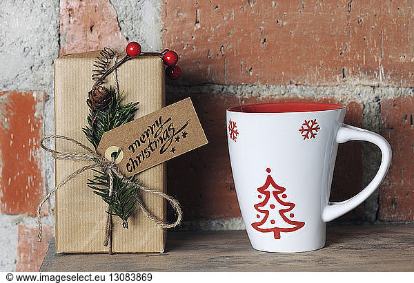 Close-up of Christmas present with mug on wooden table by brick wall