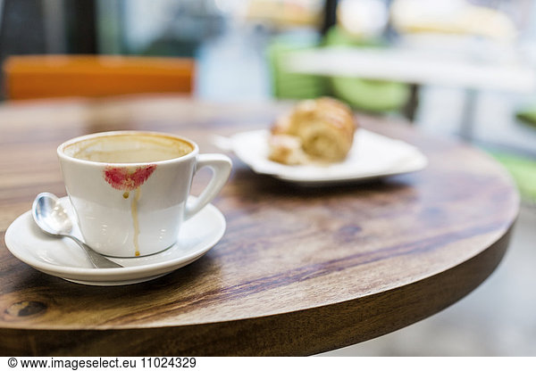 Close-up of coffee cup with lipstick kiss and croissant on table