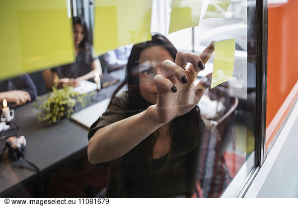 Close-up of creative businesswoman sticking adhesive note on window seen through glass