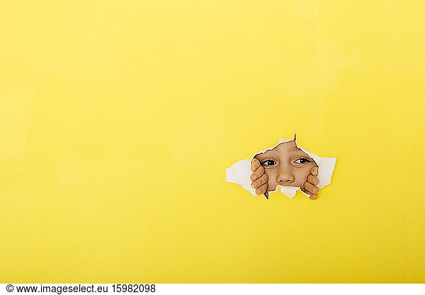Close-up of curious boy tearing yellow paper for peeking
