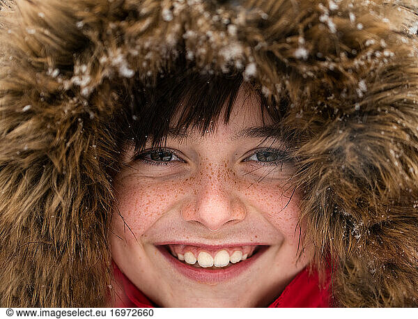 Close up of cute smiling boy in fur trimmed hood on a snowy day.