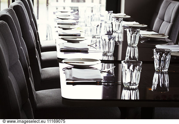 Close up of dining tables set with glasses  plates  cutlery and napkins in a restaurant.