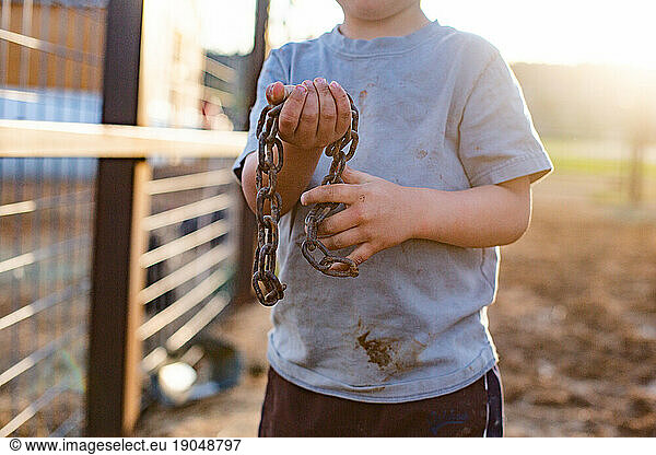 Close up of dirty boy holding rusted chain
