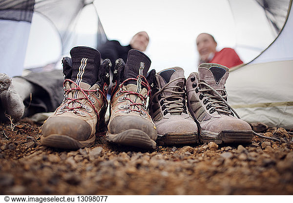 Close-up of dirty shoes with hikers relaxing in background