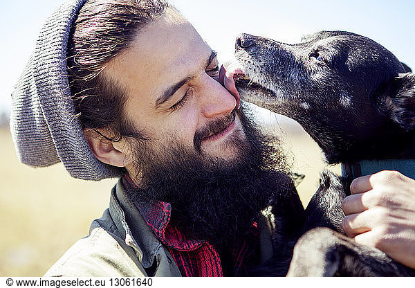 Close-up of dog licking man's face during sunny day