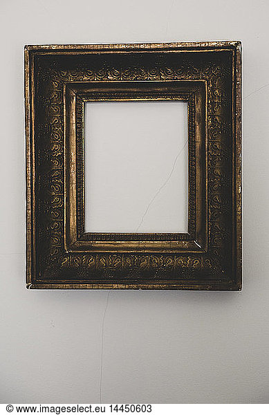 Close up of empty gilded antique picture frame on grey wall.