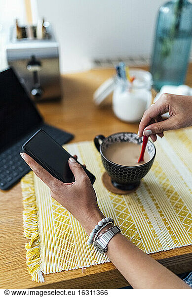 Close-up of female entrepreneur with coffee cup on desk using smart phone at home