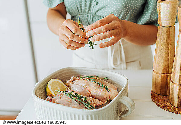 Close up of female hands adding thyme seasoning to raw chicken