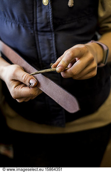 Close up of female saddler standing in workshop  working on leather strap.
