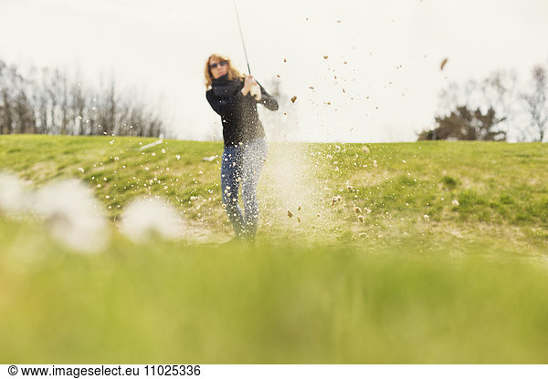 Close-up of field with woman playing golf in background at golf course