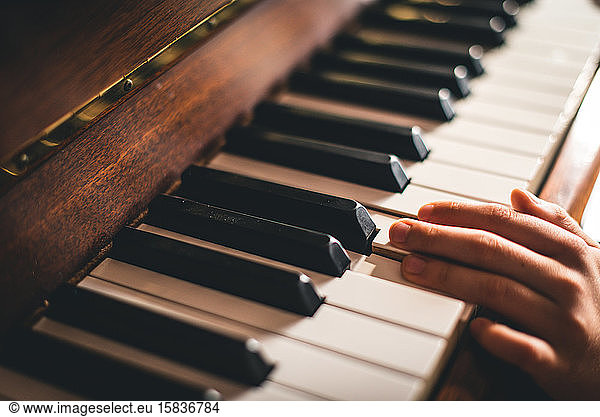 Close up of fingers of a child's hand resting on piano keys.