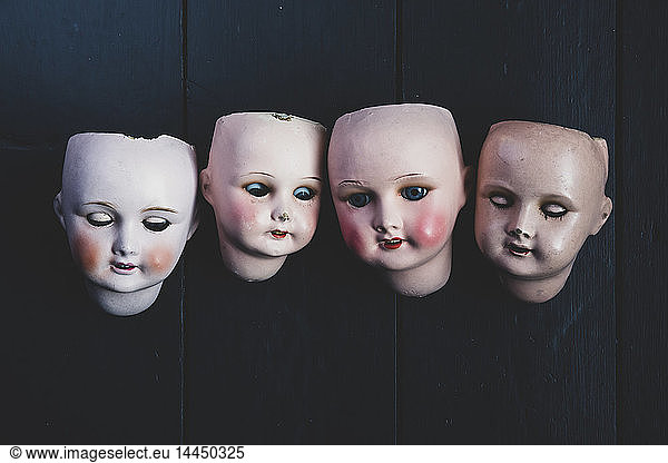 Close up of four porcelain dolls' heads on black background.