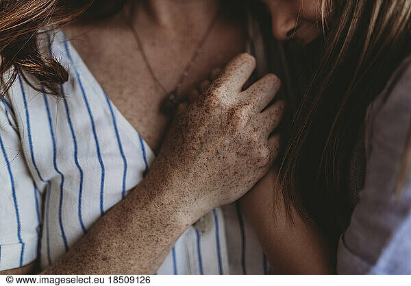 Close up of freckled mother's hand embracing daughters