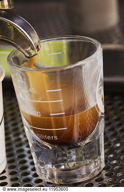 Close up of fresh brewed expresso coffee pouring into a glass from a coffee machine.