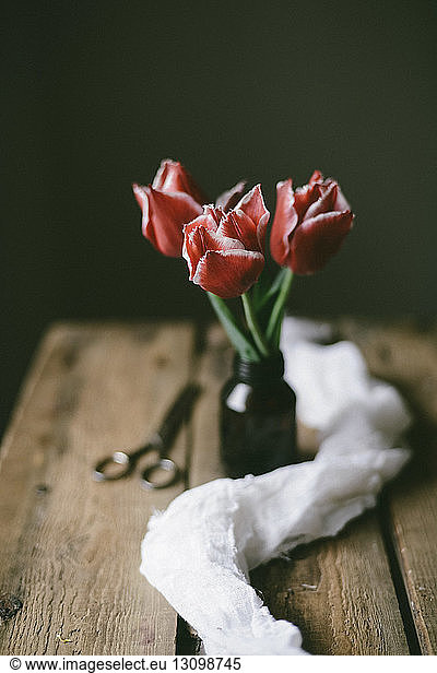 Close-up of fresh tulips in bottle by scissor and textile on wooden table
