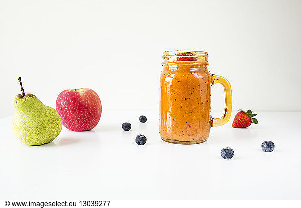 Close-up of fruits with smoothie in mason jar over white background