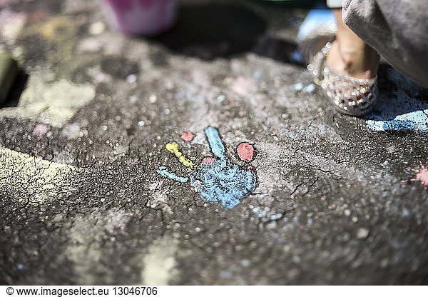 Close-up of girl by handprint on asphalt during sunny day