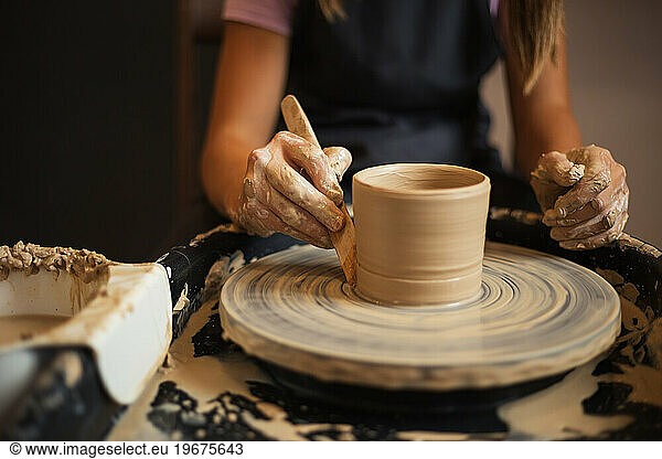 Close up of girl's hands molds clay pot spinning on pottery whee