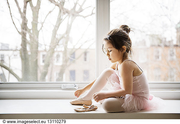 Close-up of girl wearing ballet shoes while sitting on window