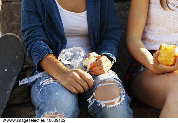 Close-up of girls eating apple while sitting on retaining wall