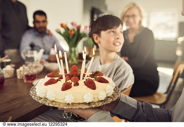 Close-up of grandfather holding birthday cake with family in background