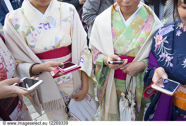 Close up of group of women wearing traditional Japanese kimonos standing side by side  holding smartphones.