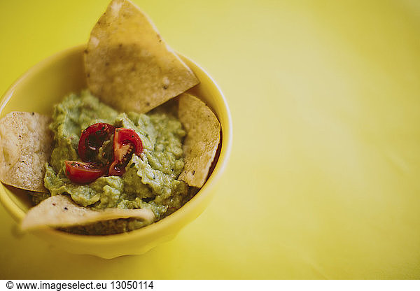 Close-up of guacamole with tortilla chips served in bowl over yellow background