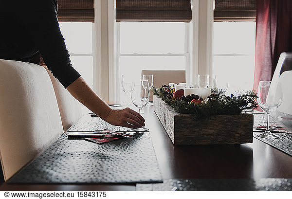 Close up of hand placing wine glass on place setting of dining table.