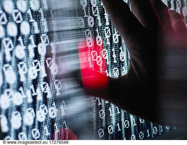 Close-up of hand touching computer screen with binary code