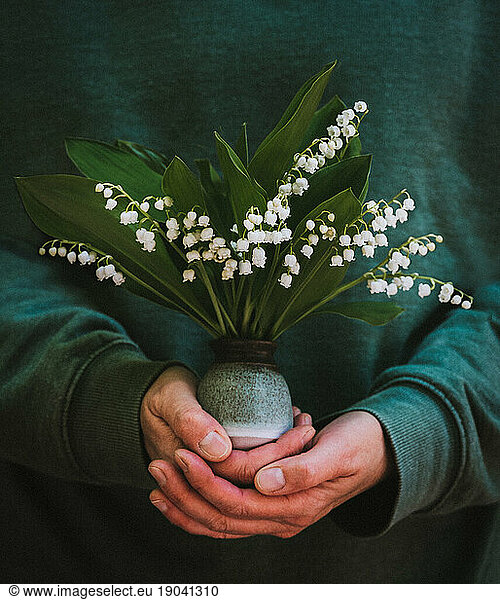 Close up of hands holding a small vase of lily of the valley flowers.