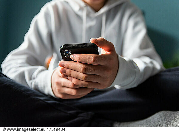 Close up of hands of teen boy in white sweater texting on phone.