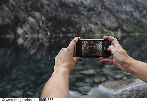 Close up of hands taking a photo with cellphone of landscape.