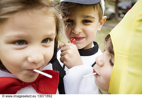 Close-up of happy children in Halloween costumes eating lollipops